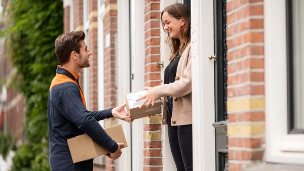 Vrouw krijgt een pakketje overhandigd door een bezorger aan de deur