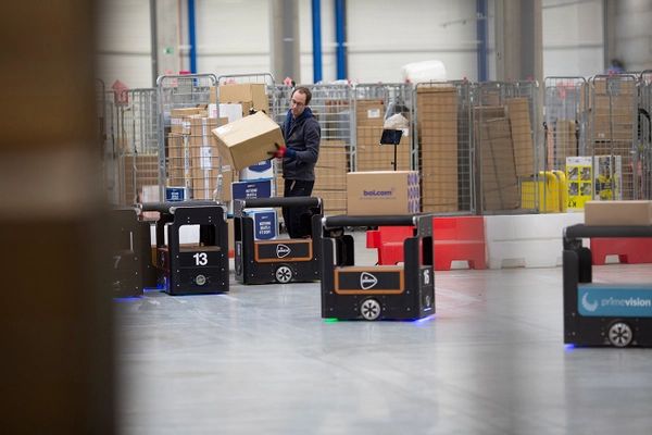 Medewerker tilt een doos terwijl autonome sorteerrobots rijden in een sorteercentrum.