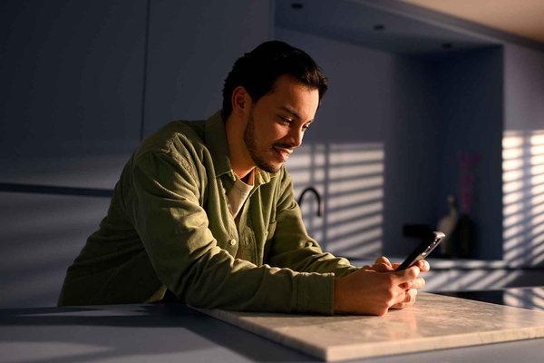 Man gebruikt een smartphone aan een keukentafel in huiselijke setting.