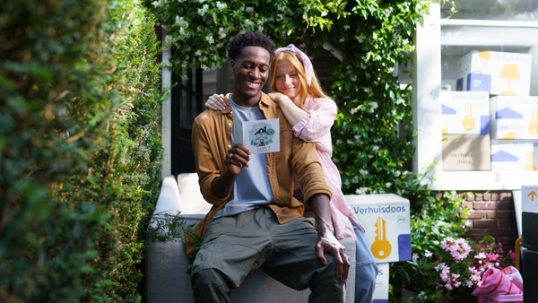 Jong stel houdt een verhuiskaartje vast, met op de achtergrond stapels verhuisdozen.