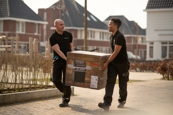 Twee bezorgers tillen samen een zwaar pakket naar een huis