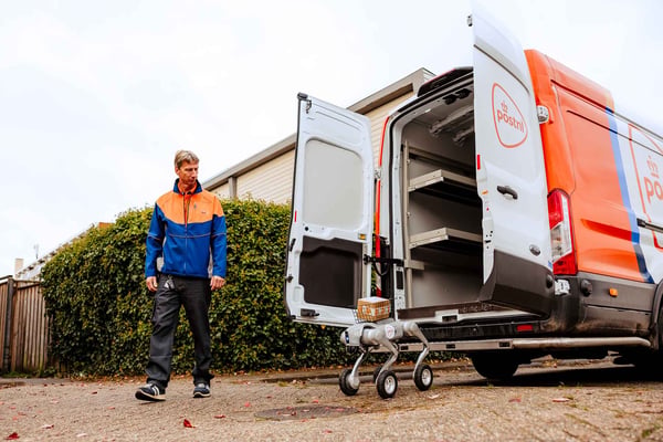 PostNL-bezorger kijkt naar een bezorgrobot die een pakket uit een bus haalt.