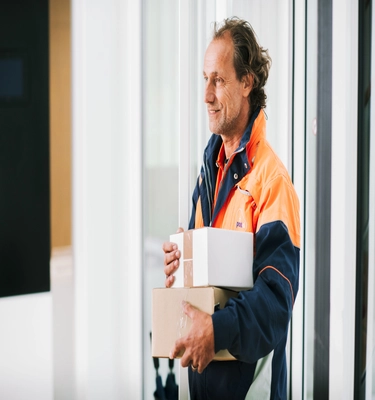 Glimlachende PostNL pakketbezorger levert twee pakketten af