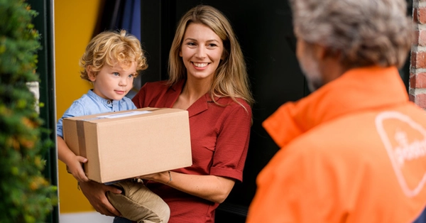 Vrouw met kind op de arm ontvangt een pakket aan de deur